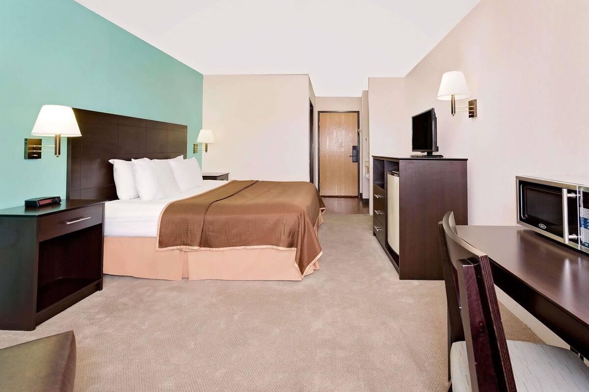 Een hotelkamer met een bed, nachtkastjes, een bureau met stoel, een televisie en een magnetron.