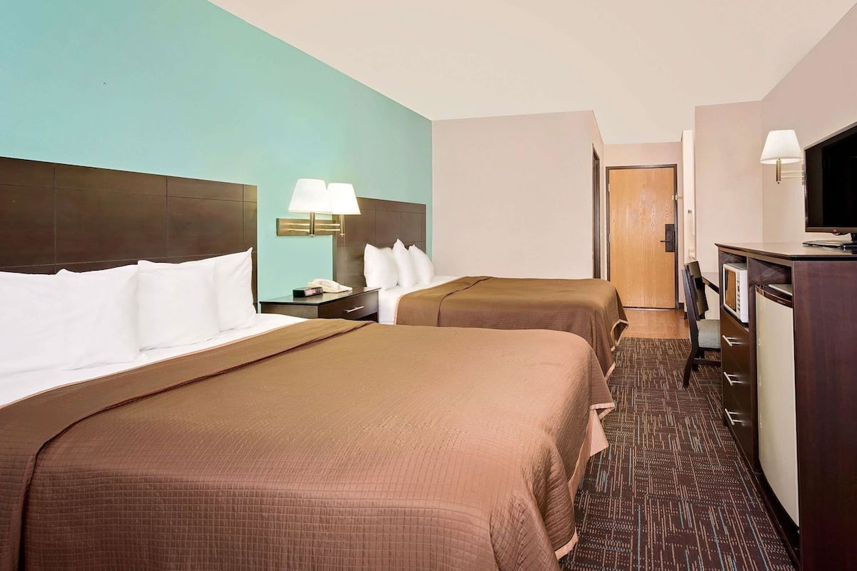 Een hotelkamer met twee bedden, een bureau met lamp, een televisie en een deur naar een andere kamer.