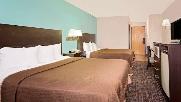 Habitación de hotel con dos camas, un escritorio con lámpara, televisión y una puerta que da a otra habitación.