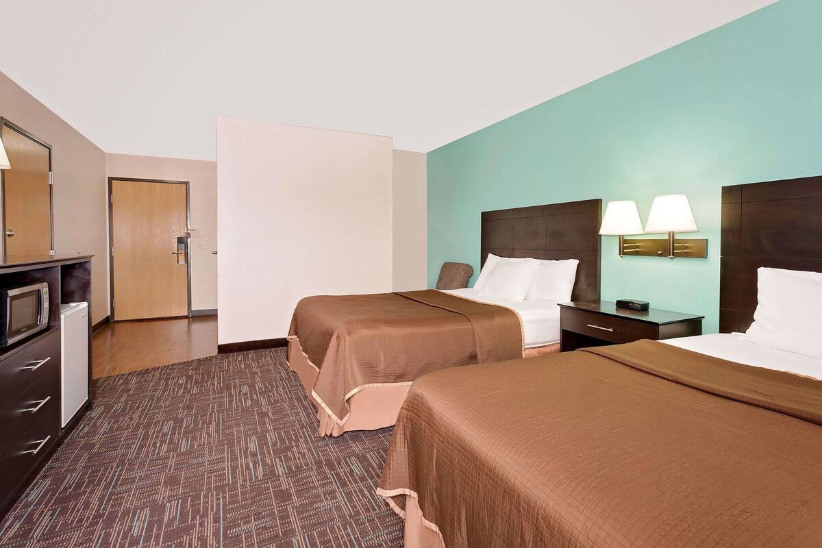 Een hotelkamer met twee bedden, een bureau met lamp, een magnetron en een deur.