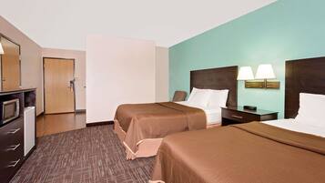 A hotel room with two beds, a desk with a lamp, a microwave, and a door.