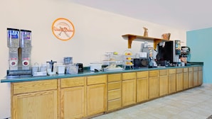 Una barra de desayuno con una máquina de café, una exposición de fruta y un reloj en la pared.