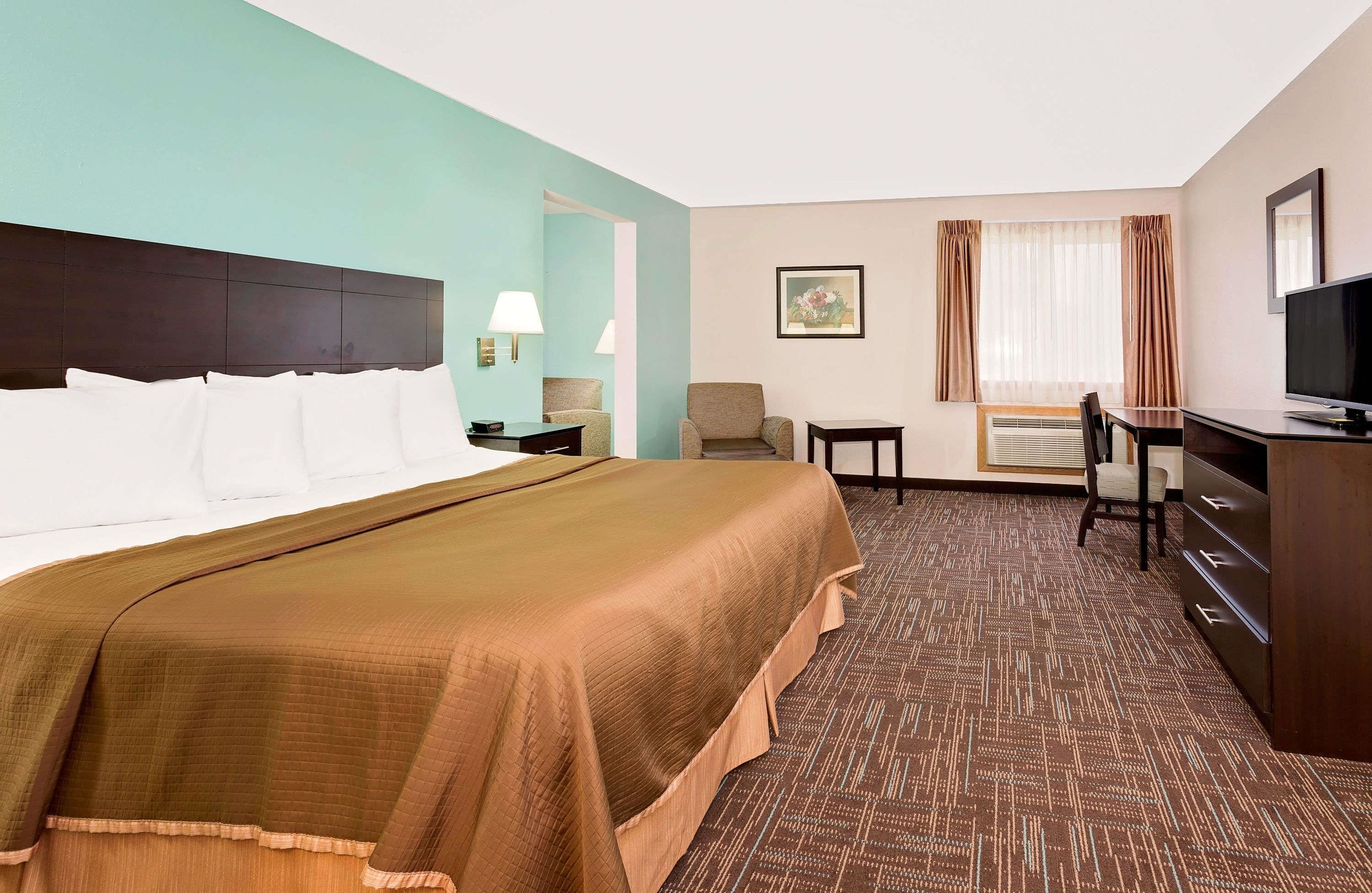 A hotel room with a large bed, a desk, a chair, a television, and a window with curtains.