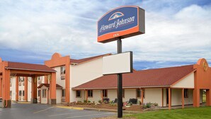 Un hotel Howard Johnson con un letrero grande, un estacionamiento y un edificio de techo rojo y paredes color beige.