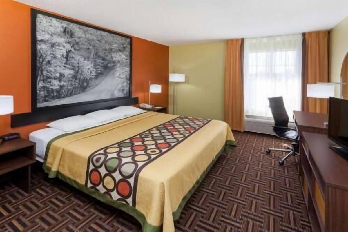 A hotel room with a bed, a desk, a chair, a TV, and a large painting on the wall.