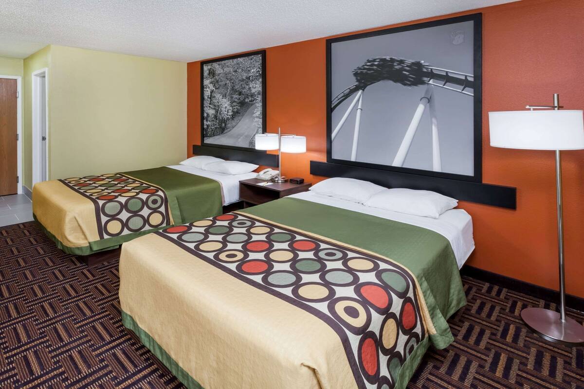 A hotel room with two beds, a nightstand, a lamp, and two framed pictures on the wall.
