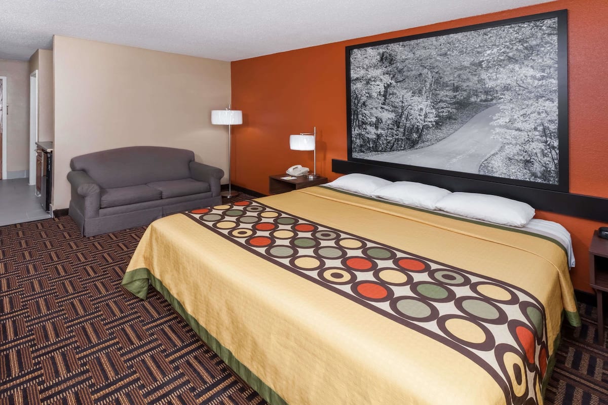 A hotel room with a bed, a sofa, a nightstand, a lamp, and a large framed picture on the wall.