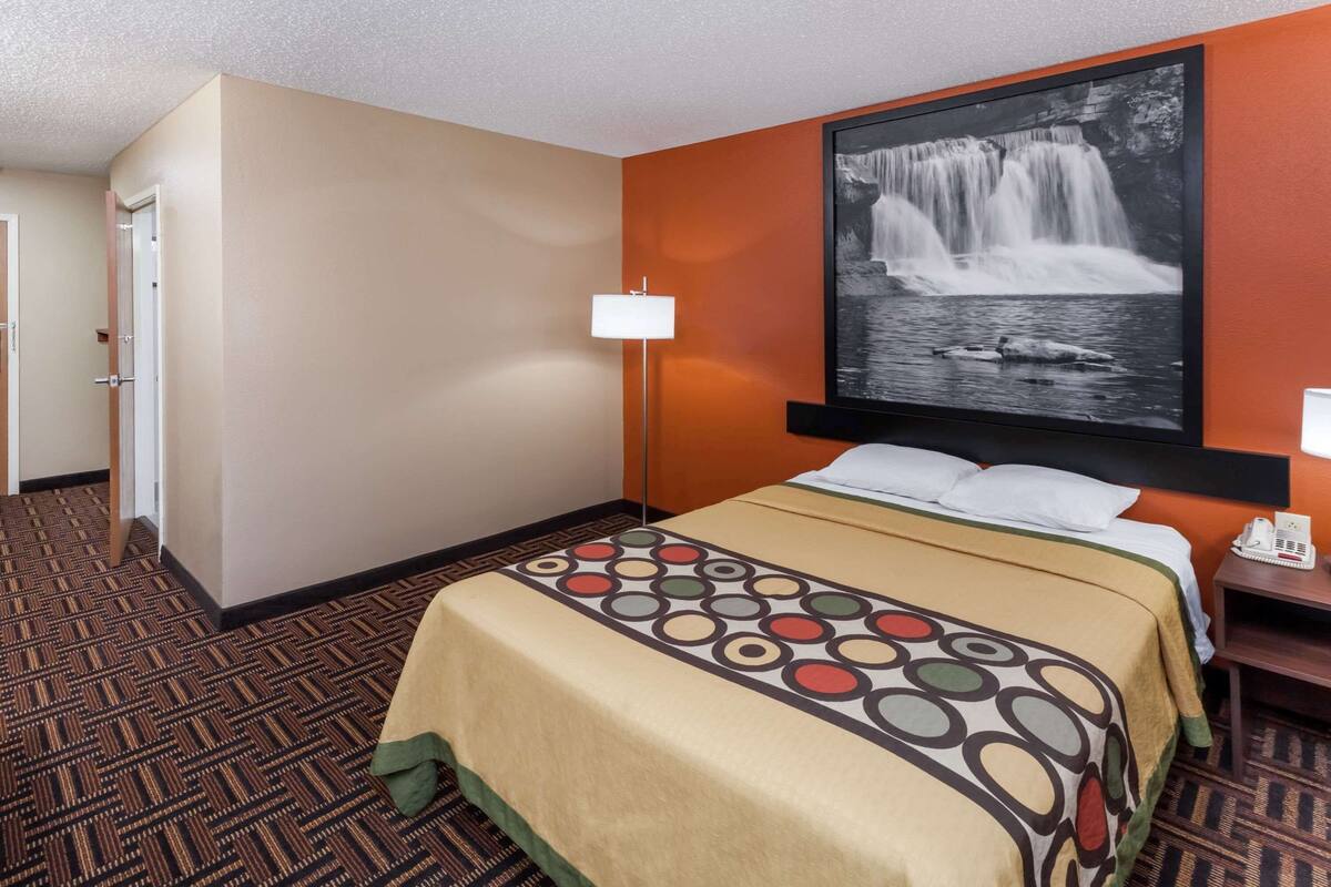A hotel room with a bed, a nightstand, a lamp, and a wall-mounted TV displaying a waterfall image.