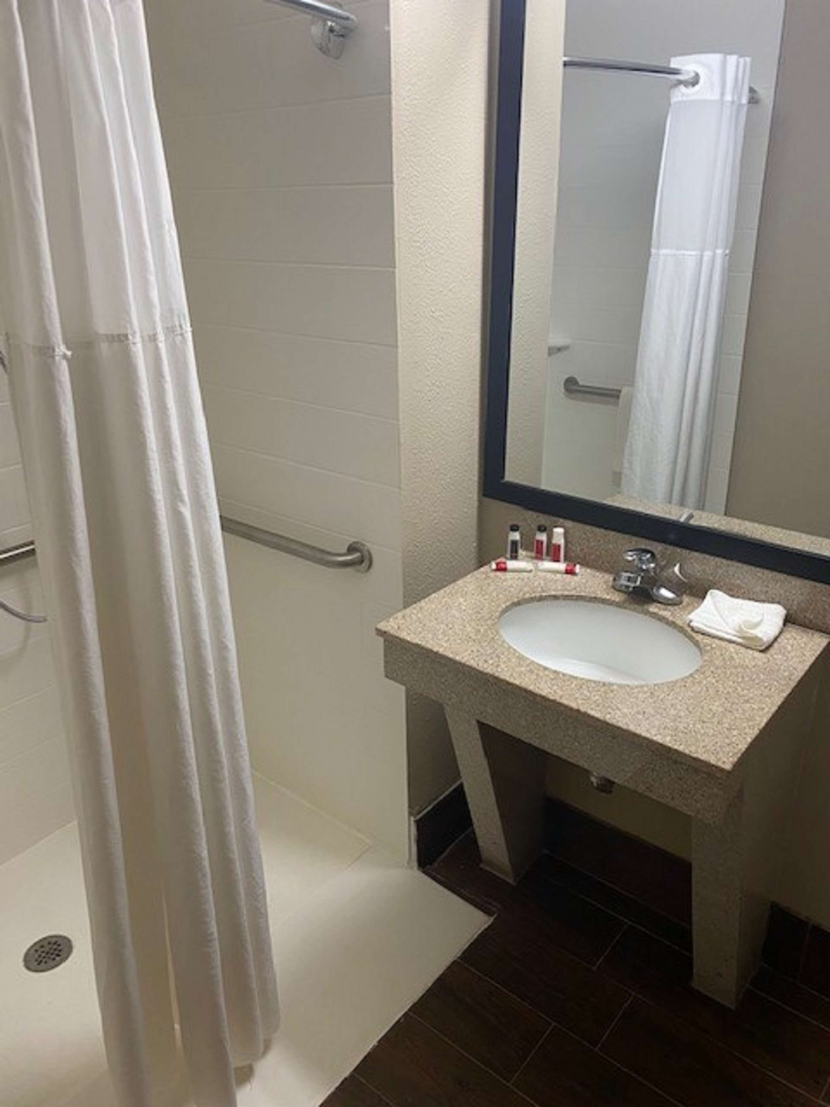 A bathroom with a white shower curtain, a sink with a mirror above it, and toiletries on the sink.