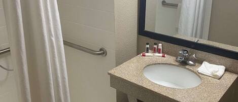 A bathroom with a white shower curtain, a sink with a mirror above it, and toiletries on the sink.