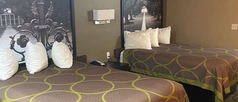 A hotel room with two beds, each with a patterned bedspread, a nightstand, a wall-mounted lamp, and a large framed picture of a park pathway.