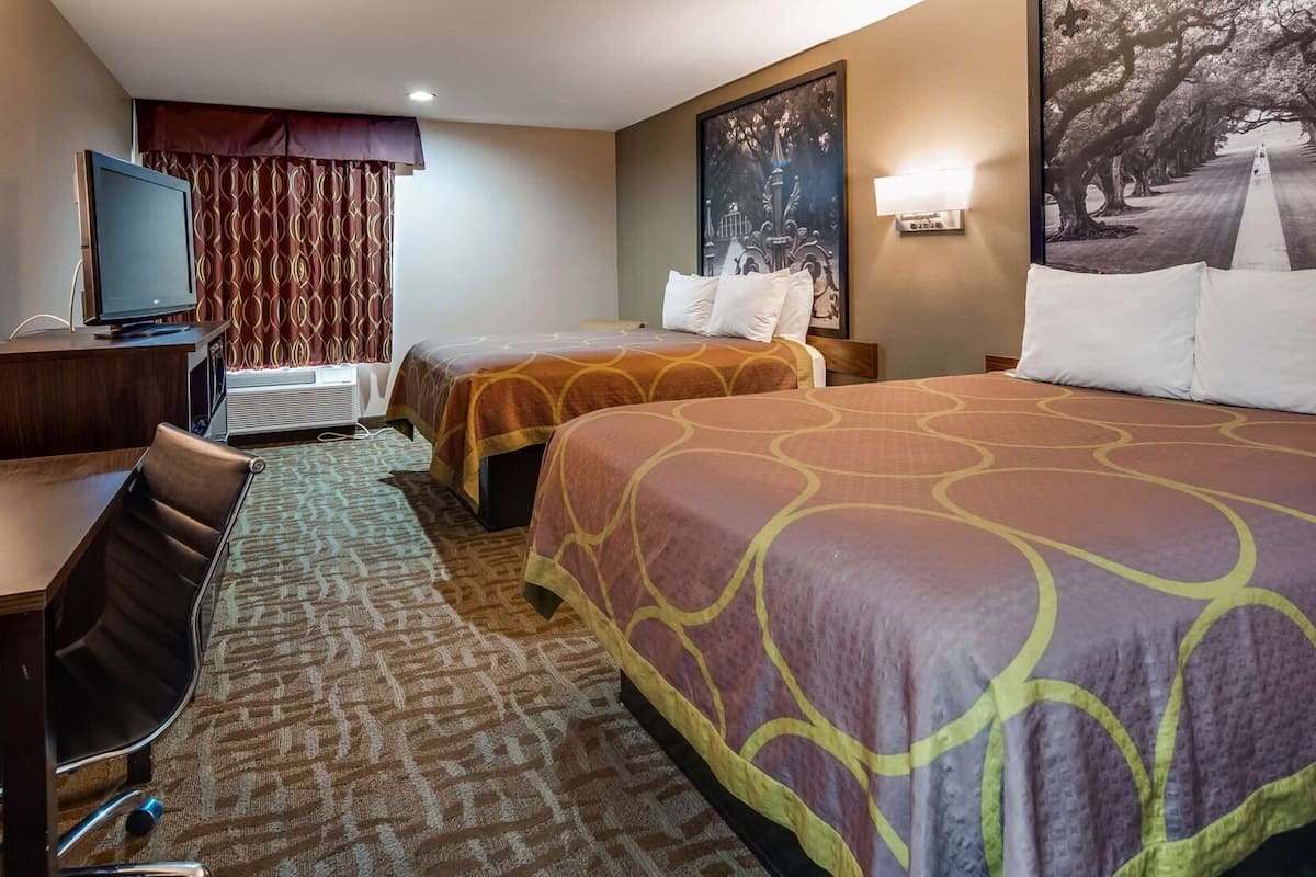 Ett hotellrum med två sängar, ett skrivbord, en tv och ett stort fönster med gardiner.
