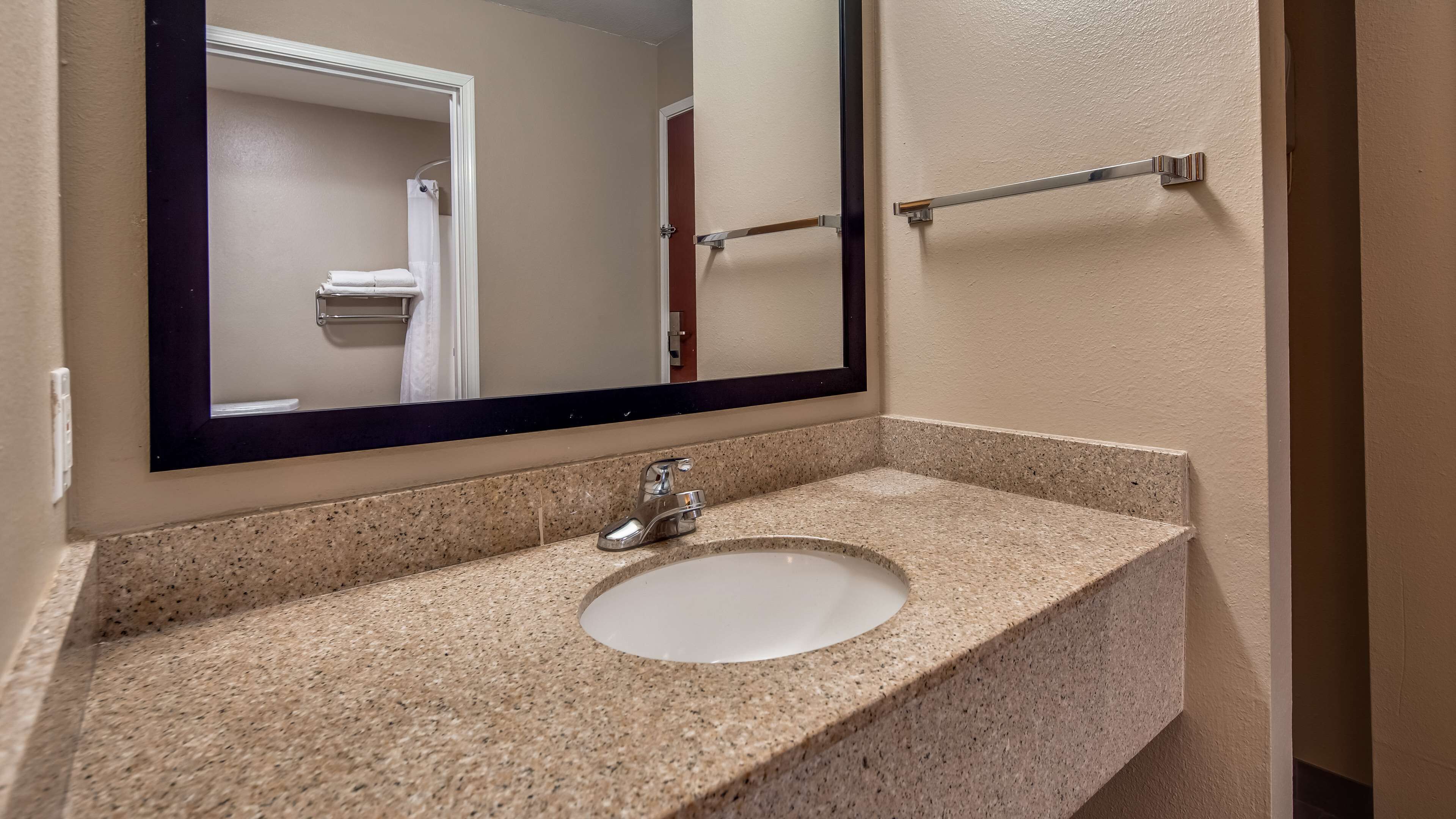 A bathroom with a granite countertop, a white sink, and a large mirror.