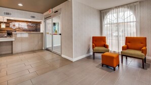 A hotel lobby with a reception desk, two armchairs, an ottoman, and a large window with sheer curtains.