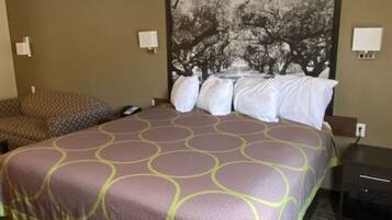 A hotel room with a large bed, a headboard with a tree mural, two bedside tables, and a patterned carpet.