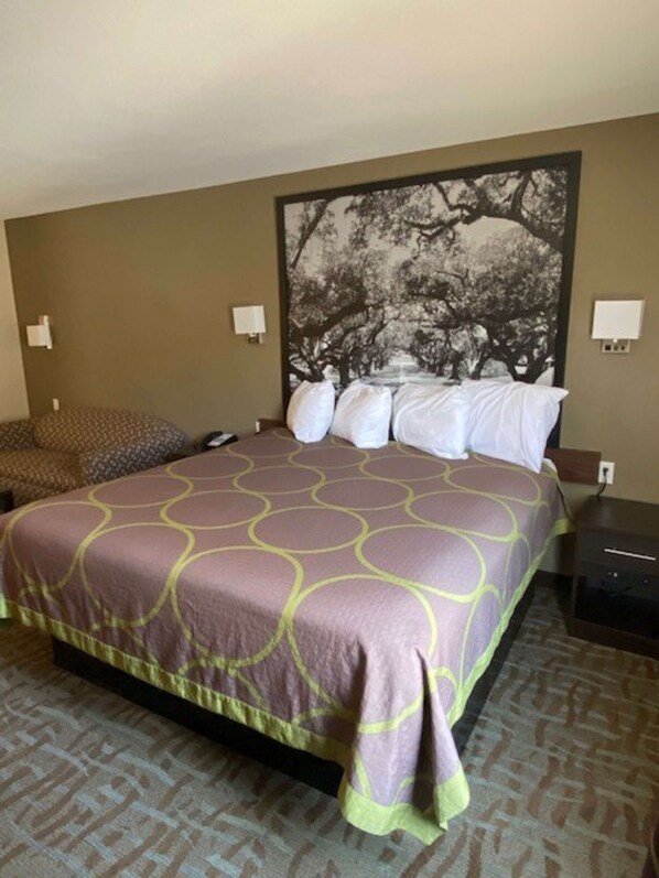 A hotel room with a large bed, a headboard with a tree mural, two bedside tables, and a patterned carpet.