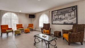 A hotel lobby with a large framed map, several orange armchairs, a glass coffee table, and a television mounted on the wall.