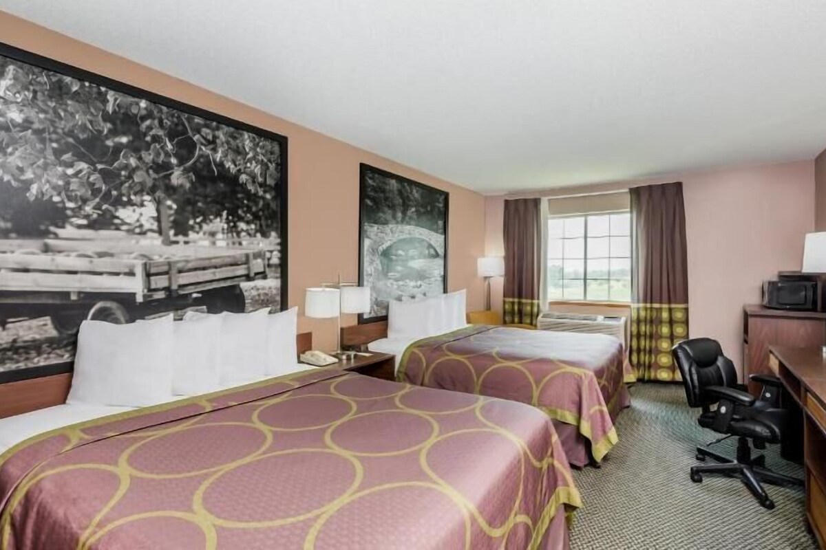 A hotel room with two beds, a desk, a chair, a television, and large windows.
