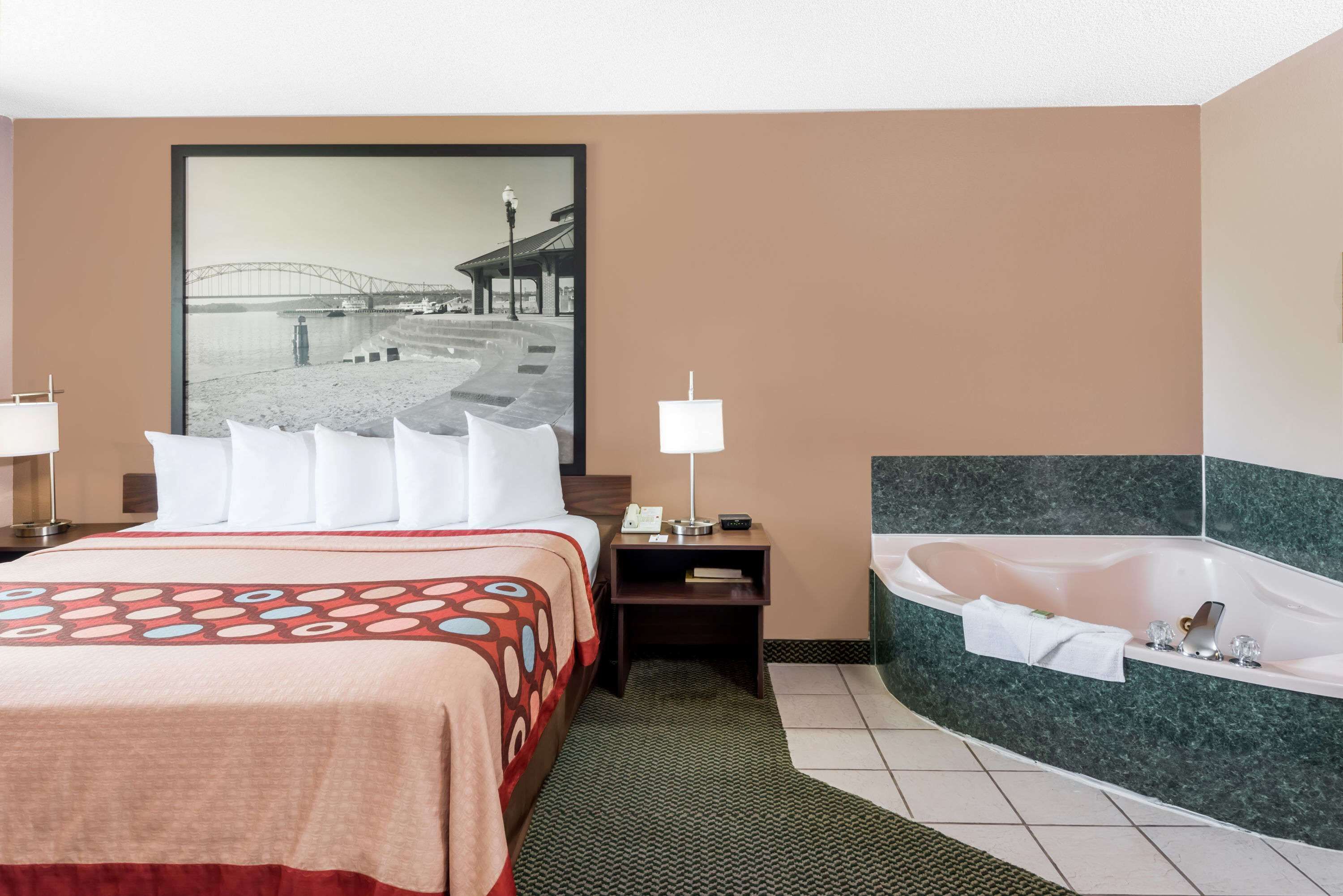 Habitación de hotel con cama, una gran foto enmarcada de un puente, escritorio con lámpara y baño independiente con bañera.