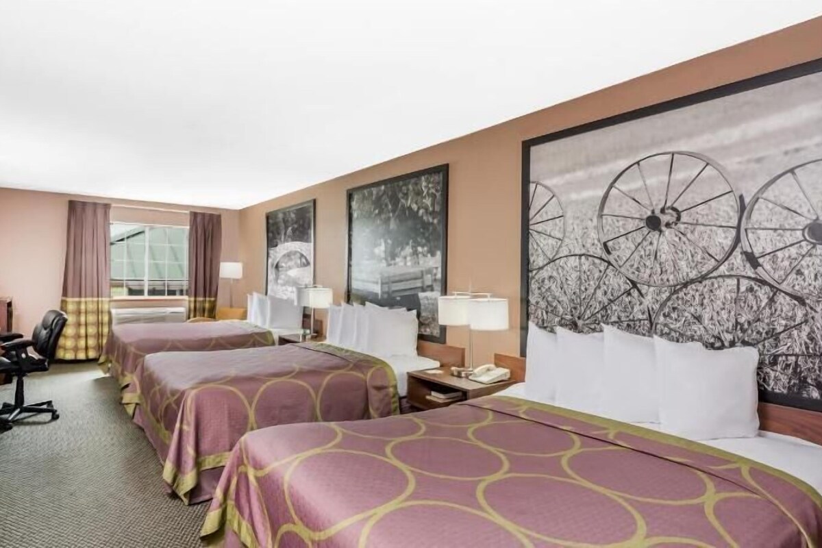 A hotel room with two beds, a desk with a computer, a chair, a TV, and artwork on the walls.