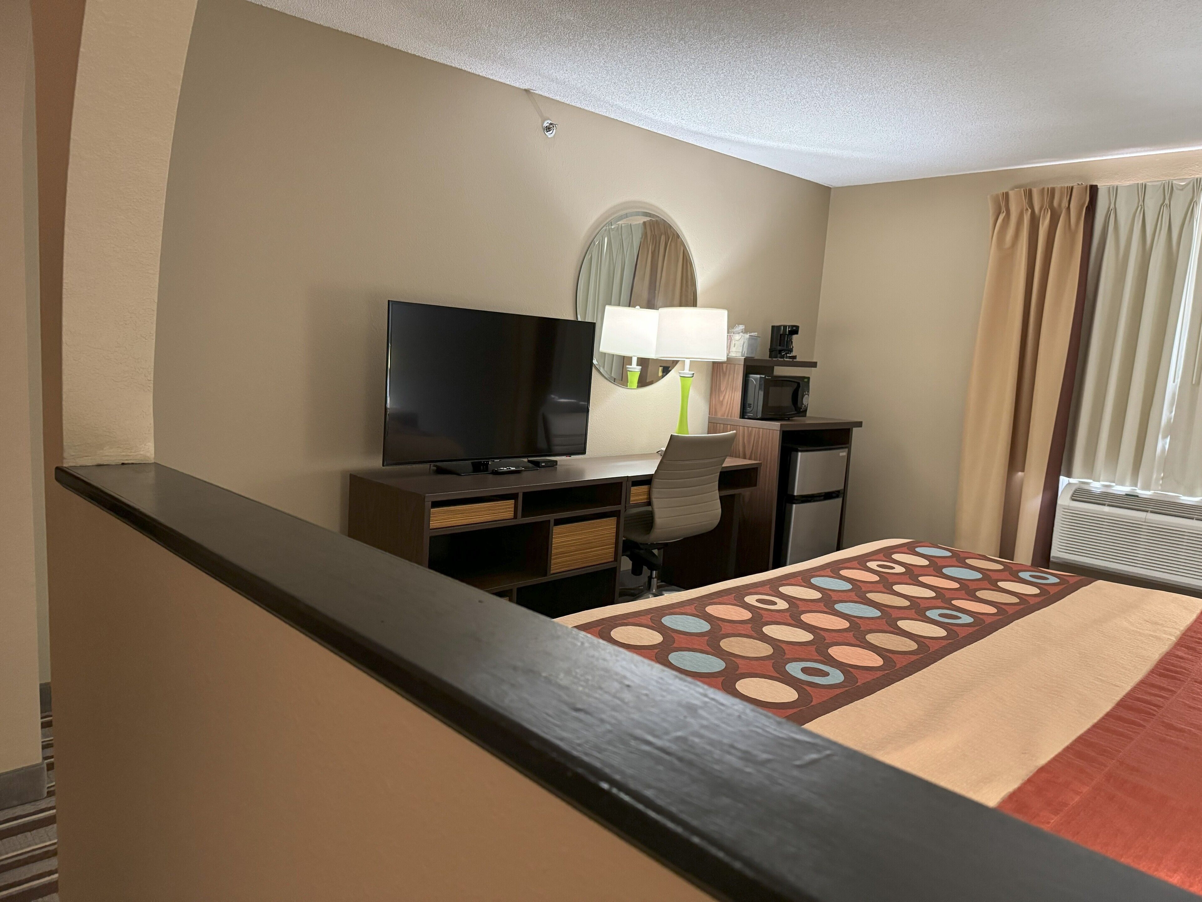 Habitación de hotel con una cama, un escritorio con televisor, un microondas y un refrigerador pequeño.