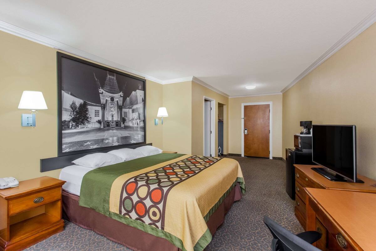 Een hotelkamer met een bed, een bureau met een televisie, twee lampen en een groot wanddecoratie.