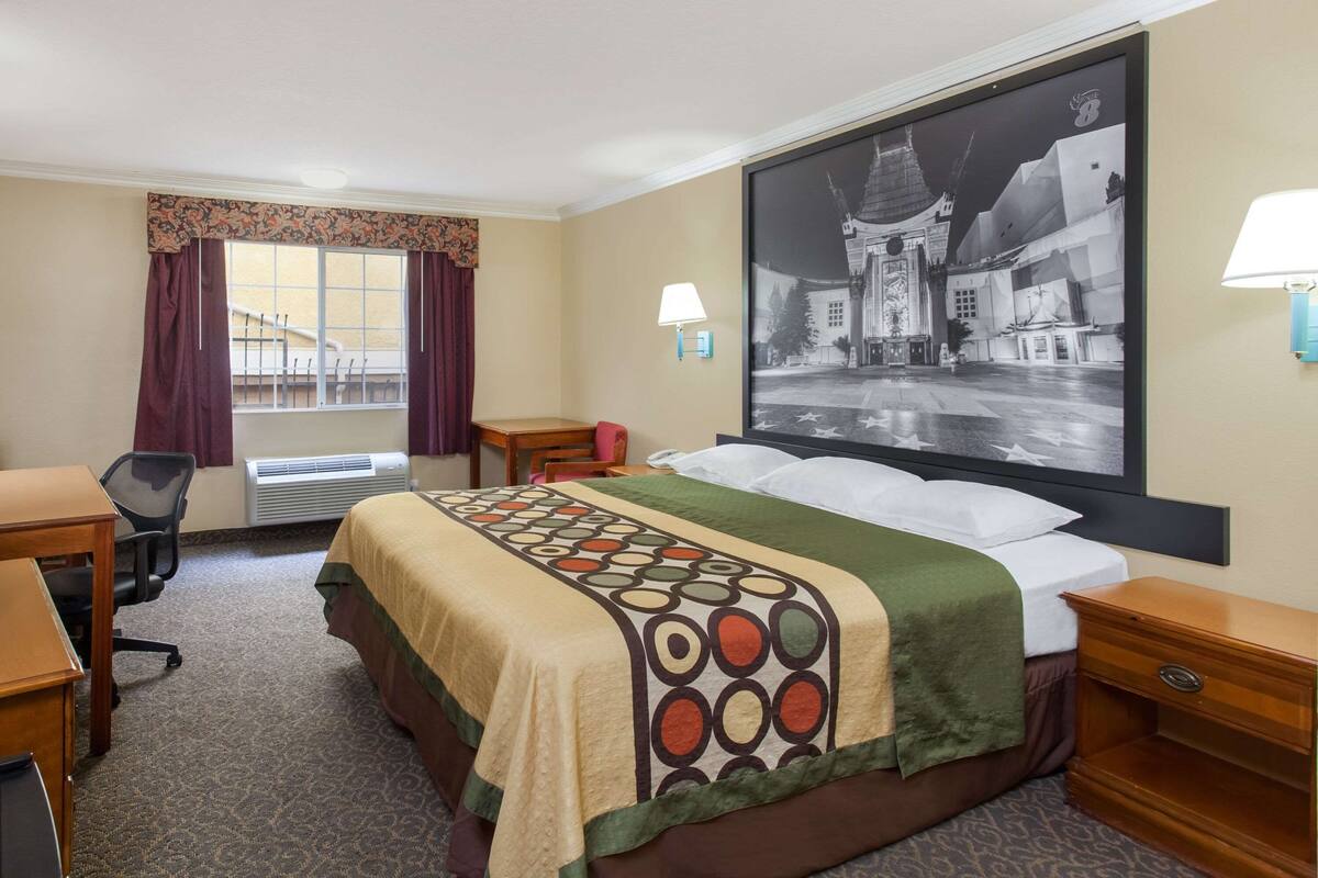 A hotel room with a bed, desk, chair, and a large framed picture on the wall.