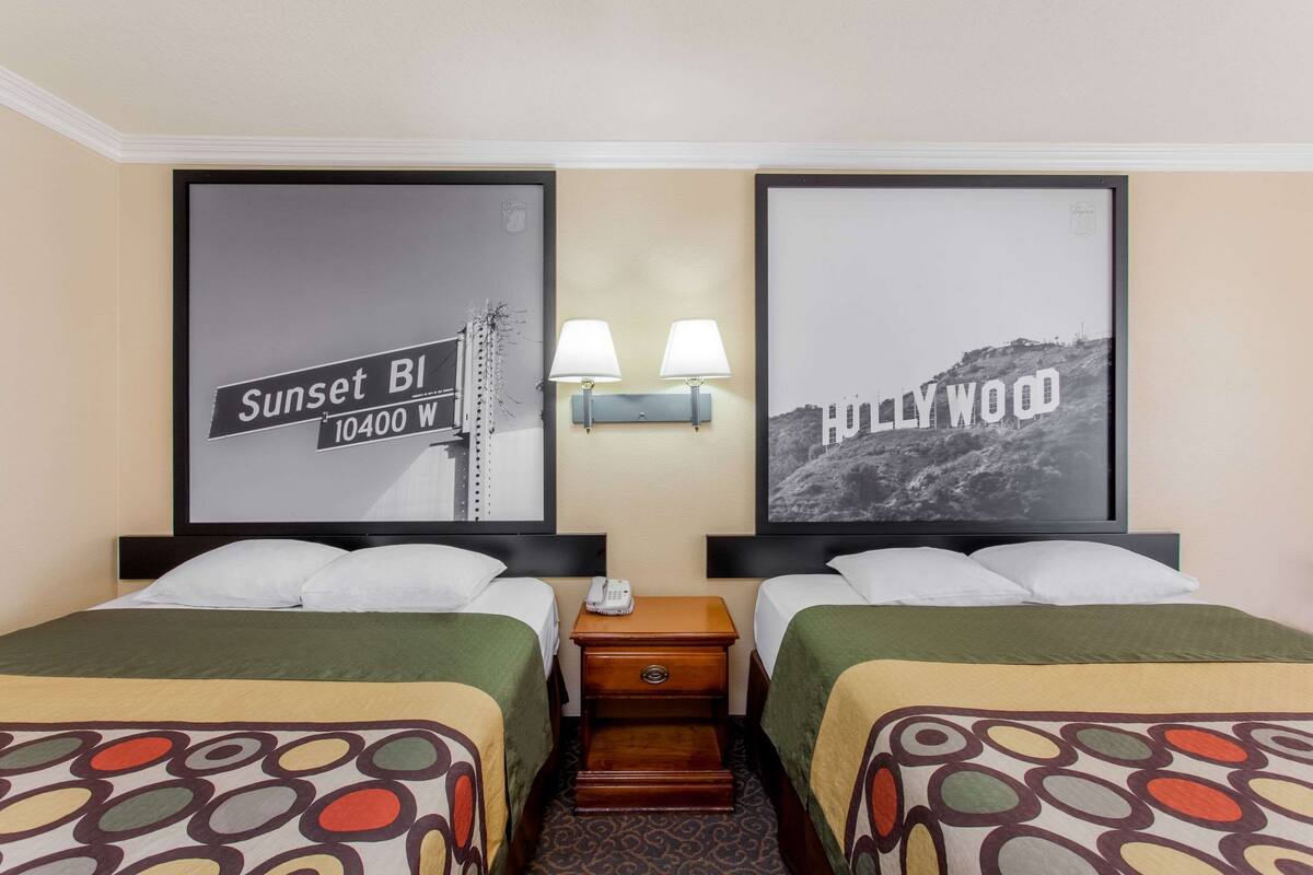A hotel room with two beds, a nightstand with a lamp, and two framed pictures on the wall.