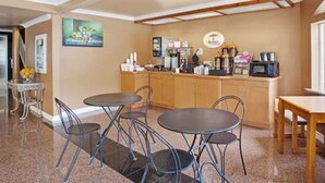 A hotel room with a kitchenette, two round tables with chairs, a painting on the wall, and a wooden cabinet. - Super 8 by Wyndham Los Angeles Downtown (Los Angeles)