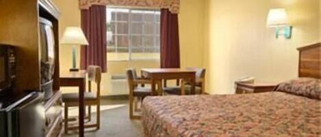 Quarto de hotel com cama, escrivaninha, cadeira, televisão e janela com cortinas.