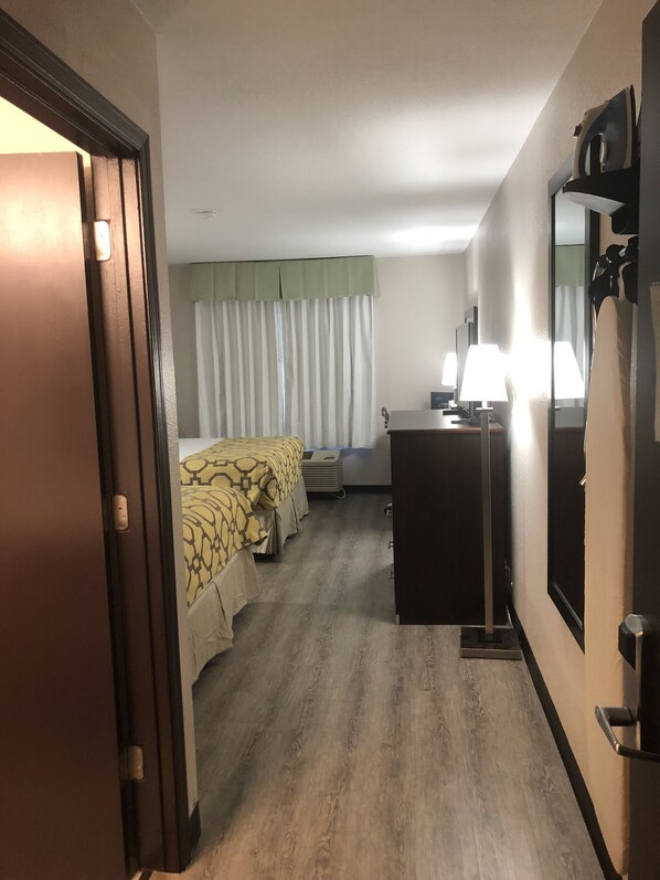 A hotel room with a bed, a desk, a dresser, and a mirror.