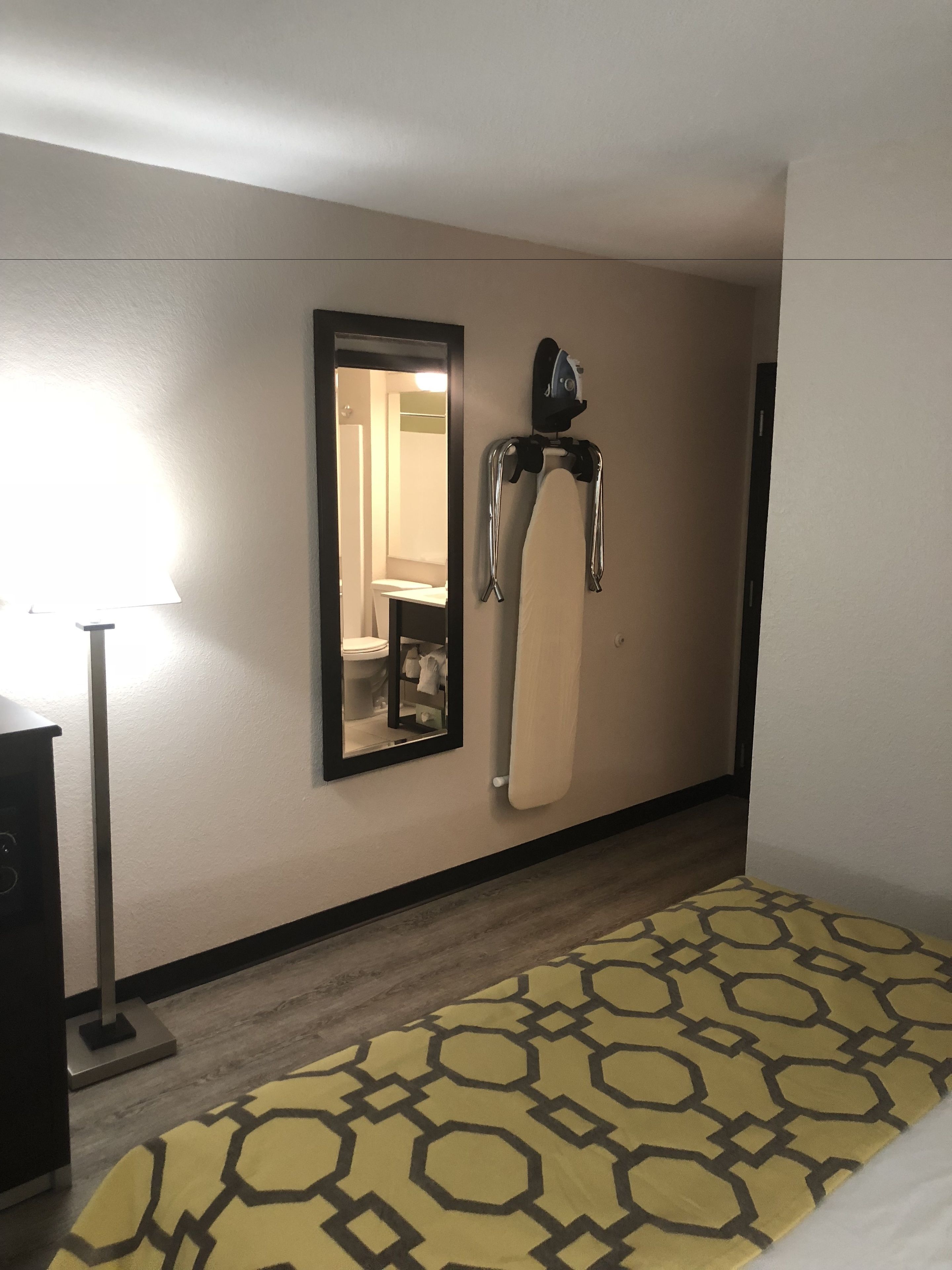 Une chambre d’hôtel équipée d’un lit, d’un miroir, d’une planche à repasser et d’une lampe.