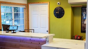 Una zona de recepción con mostrador de madera, un monitor de computadora, un reloj de pared y una cámara de seguridad.