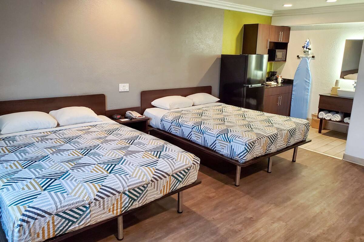 Une chambre d’hôtel avec deux lits, un plancher en bois, une kitchenette et une salle de bain visible au fond.