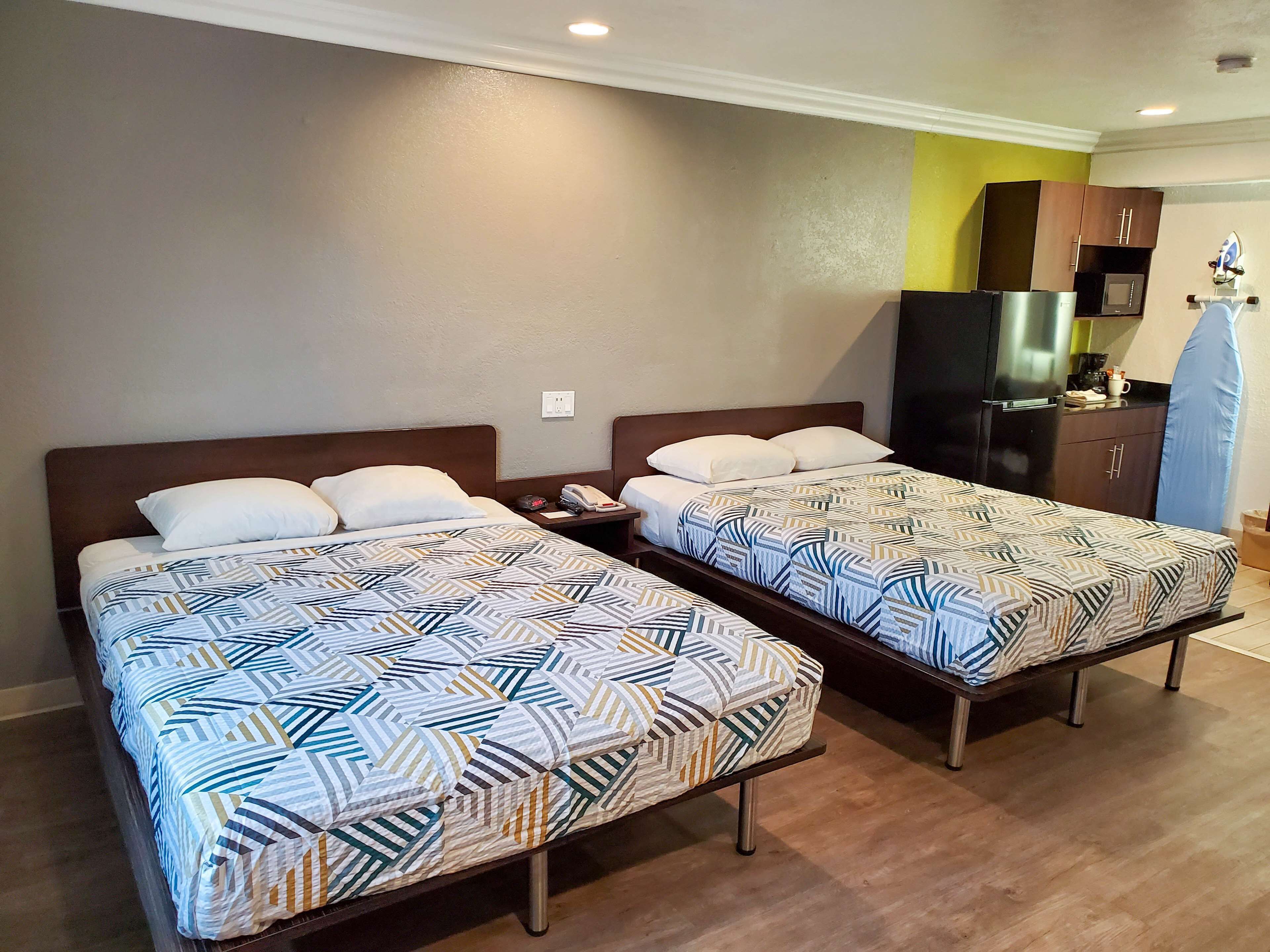 Two single beds with patterned bedding, a small bedside table, a telephone, and a microwave in a compact room with wooden flooring and a yellow accent wall.