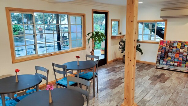 Interior de un restaurante con mesas redondas, sillas con cojines azules, ventanas amplias y una exhibición de aperitivos.