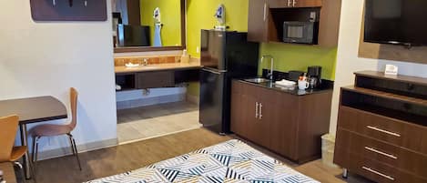 Una camera d'albergo compatta con un letto, una scrivania, angolo cottura e televisione.