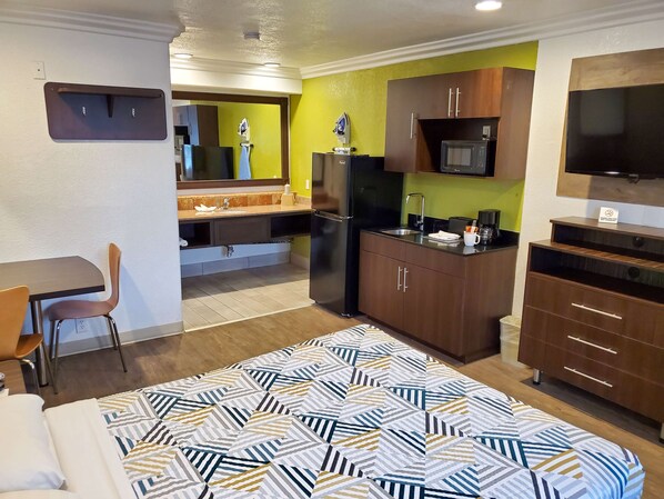 Habitación de hotel compacta con cama, escritorio, kitchenette y televisor.