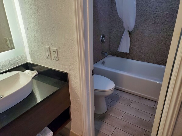 Un baño con lavamanos, inodoro y bañera blancos. Hay una toalla colgada en la pared.