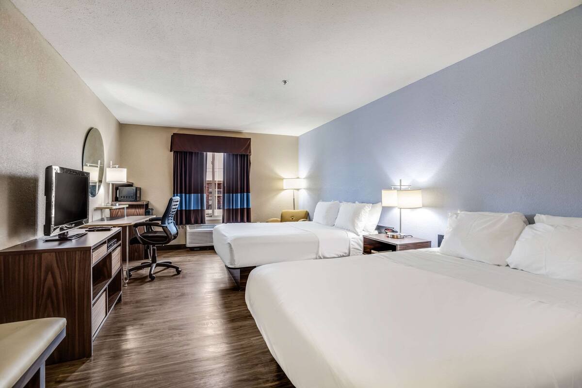 A hotel room with two beds, a desk with a computer, a TV, and a chair.