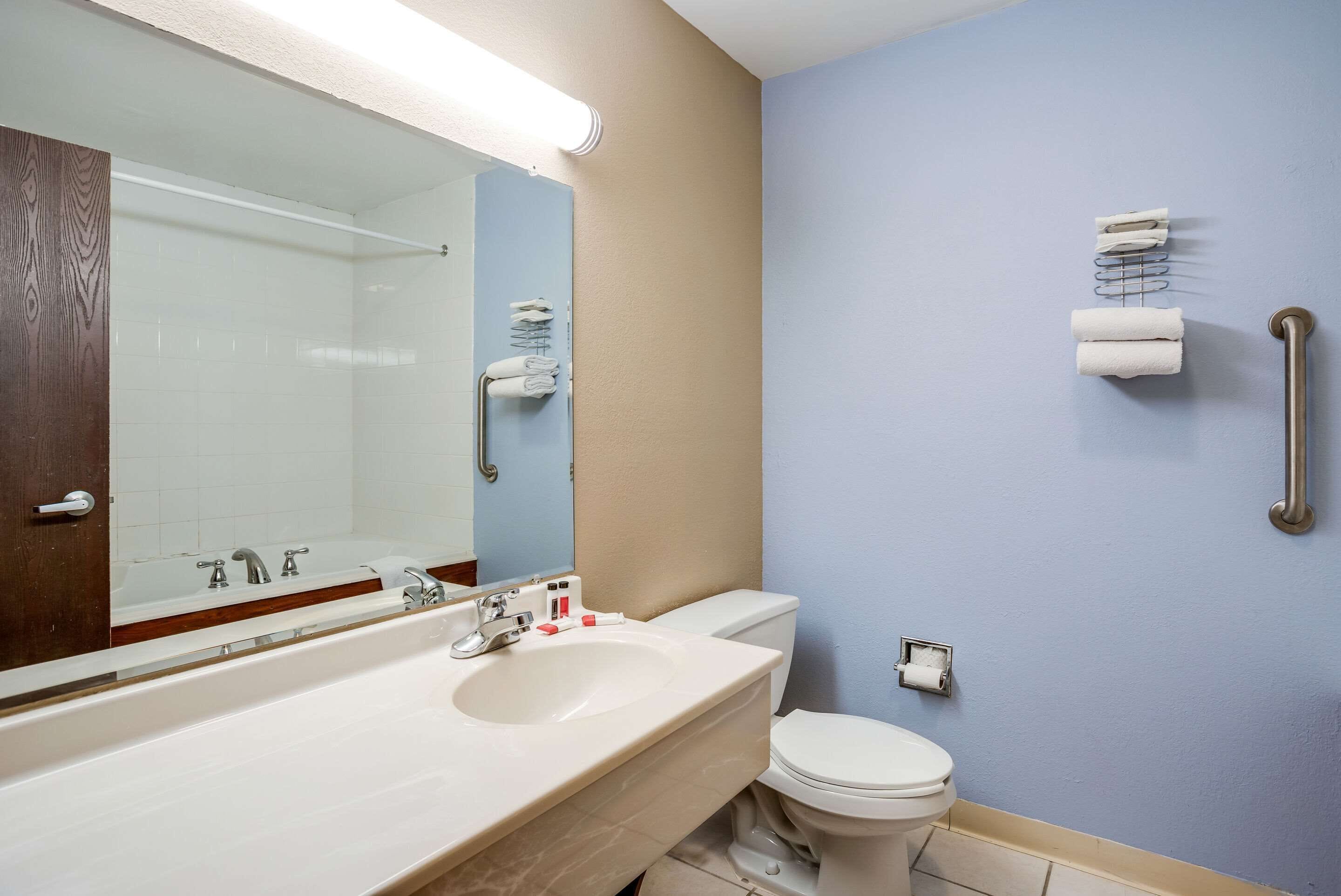 A bathroom with a white sink, mirror, and toilet. There is a towel rack with towels and a paper towel dispenser.