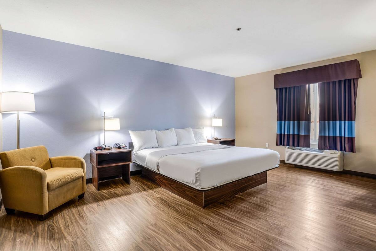 A hotel room with a bed, nightstands, a lamp, a chair, and a window with curtains.