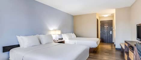 A hotel room with two beds, a desk, a TV, and a wooden floor.