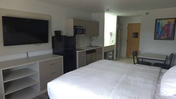 Habitación de hotel con cama, escritorio, televisor, refrigerador, microondas y lavamanos.