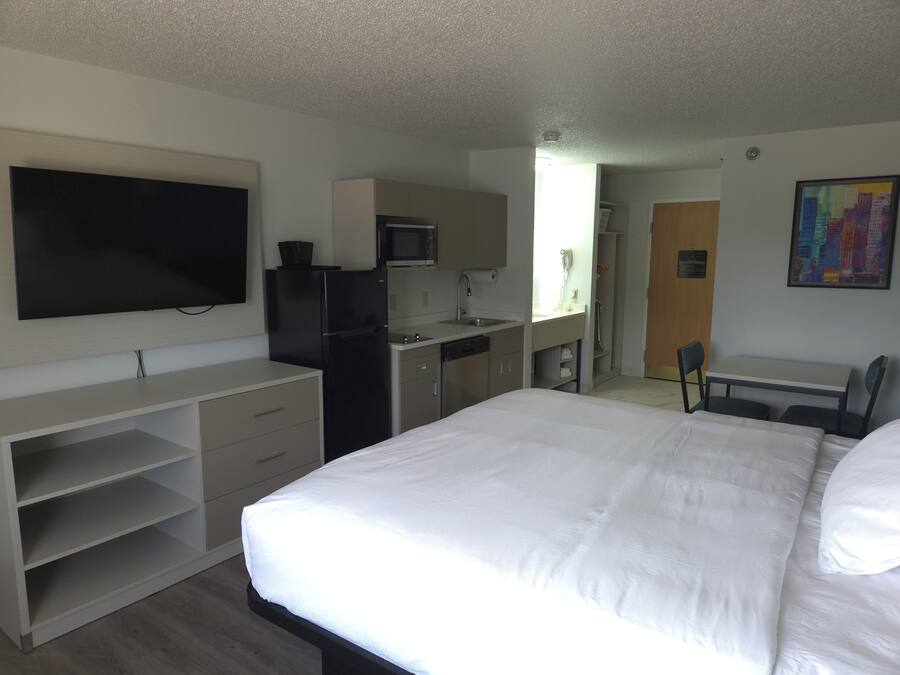 A hotel room with a bed, a desk, a TV, a refrigerator, a microwave, and a sink.