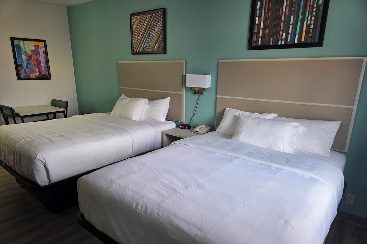A hotel room with two beds, a desk, and a chair.