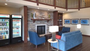 A lobby with a stone fireplace, blue seating, and a refrigerator stocked with beverages. - MainStay Suites LeClaire - Quad Cities (Le Claire)