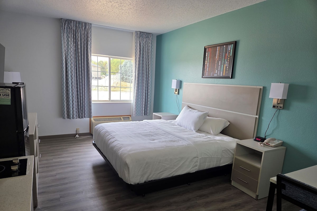 A hotel room with a bed, bedside tables, a desk, a lamp, a heater, and a window with curtains.