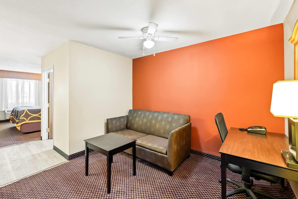 A hotel room with a sofa, a small table, a desk with a chair, and a ceiling fan.