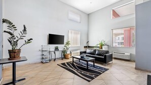 A modern living room with a black leather sofa, a flat-screen TV, and a large window with blinds. - Super 8 by Wyndham Marana/Tucson Area (Tucson)